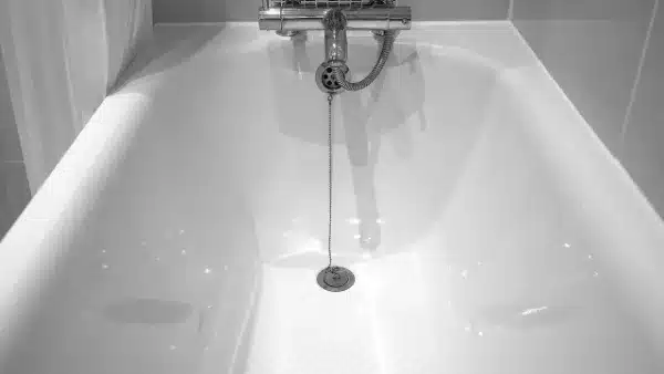 A white bathtub with a central plug hole, attached to a chain, under a metal faucet, is designed for easy drain clearing.