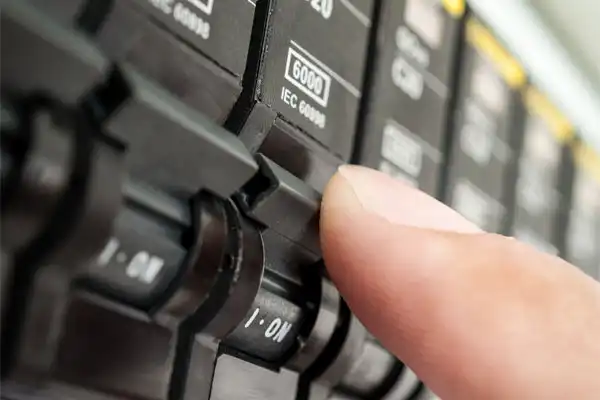 A finger touching a switch on a circuit breaker panel, with labels indicating electrical specifications.