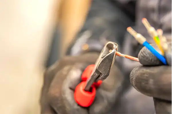 Close-up of a person in black gloves using red-handled diagonal pliers to cut copper wiring.