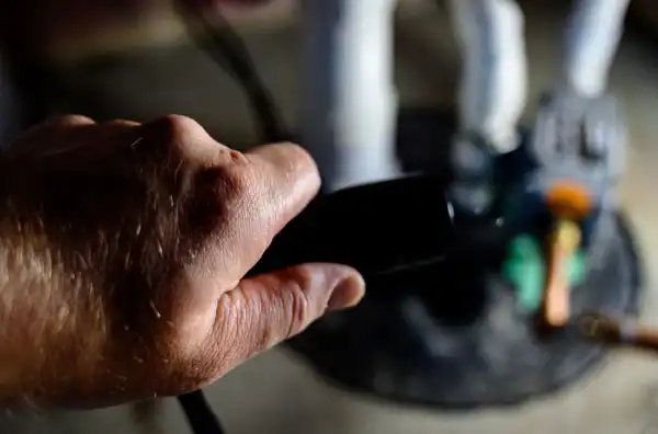 A hand gripping a black handle near a figurine on a round black base with tools and objects blurred in the background.