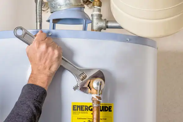 Person using a wrench on a water heater pipe, with an EnerGuide label visible.
